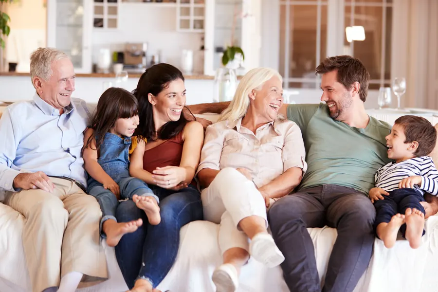 Drei Generationen einer Familie sitzen lachend auf einem Sofa