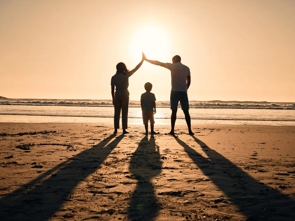 Familie formt am Strand ein Dach mit den Armen