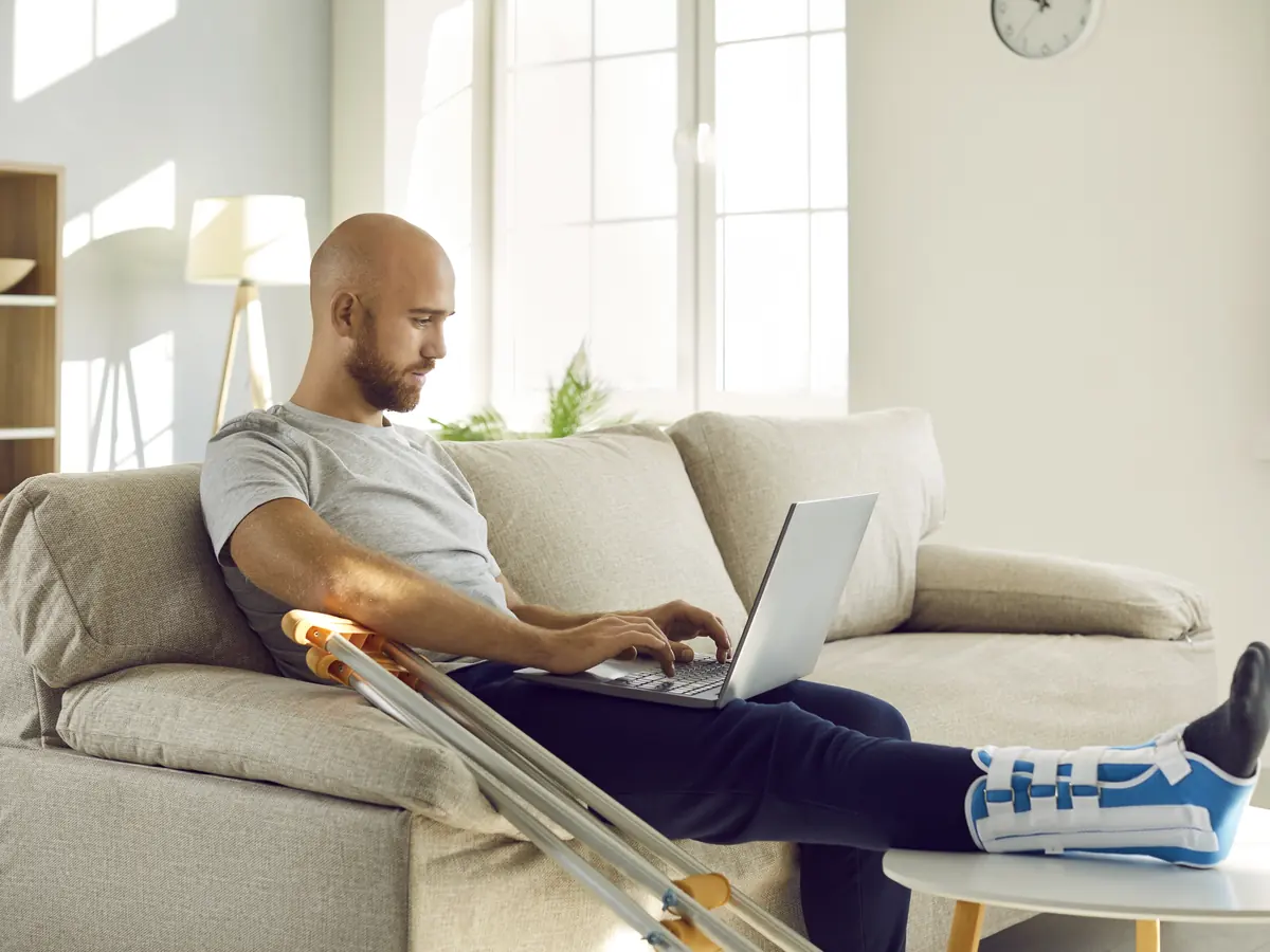 Mann mit Gipsbein arbeitet vom Sofa aus am Laptop