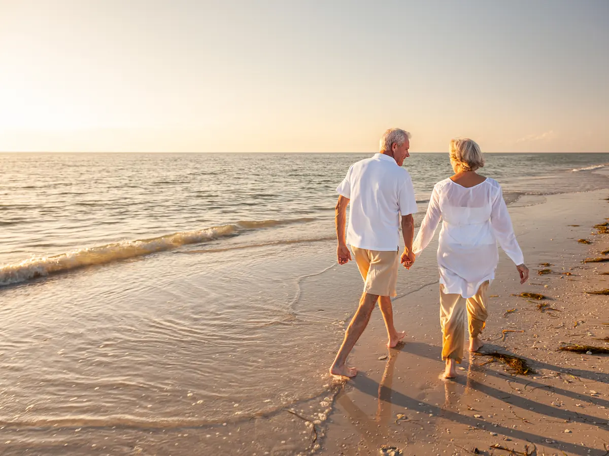 Älteres Paar spaziert Hand in Hand am Strand